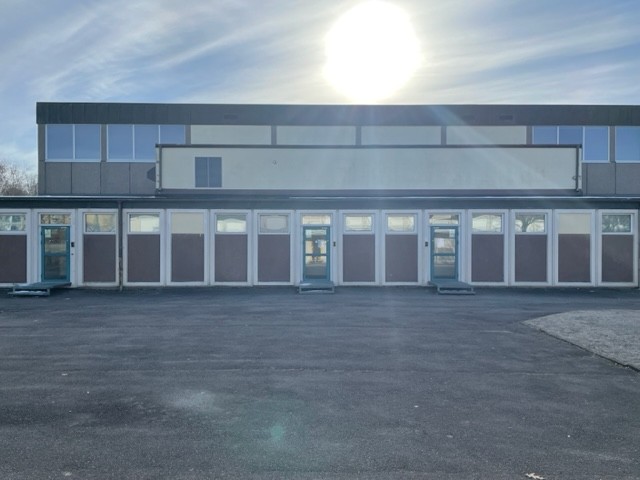 Stor grå byggnad med vita spröjs runt fönster och dörrar. Stor gul/vit sol som lyser över byggnaden.