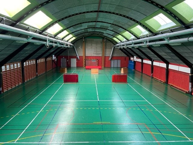 Ett grönt golv med färgade streck över golvet. Valvat tak, vita armaturer som hänger i taket.