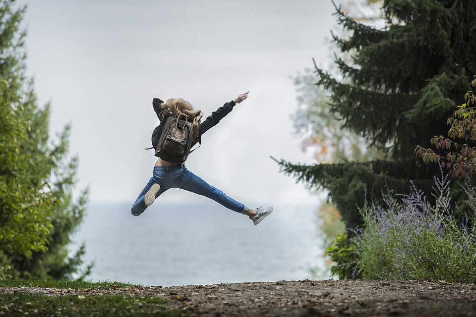En bild bakifrån på en ungdom som hoppar upp i luften och kickar ut med ett ben. Bakgrund en grusväg genom ett skogsparti.