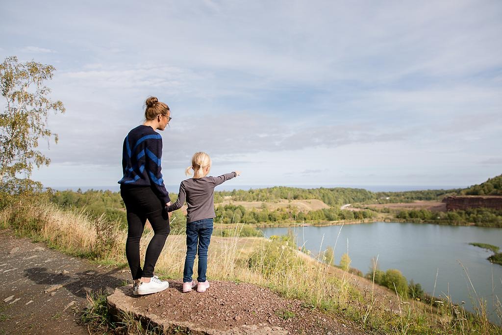 En vuxen och ett barn står och kikar ut över Stenbrottet på Kinnekulle.