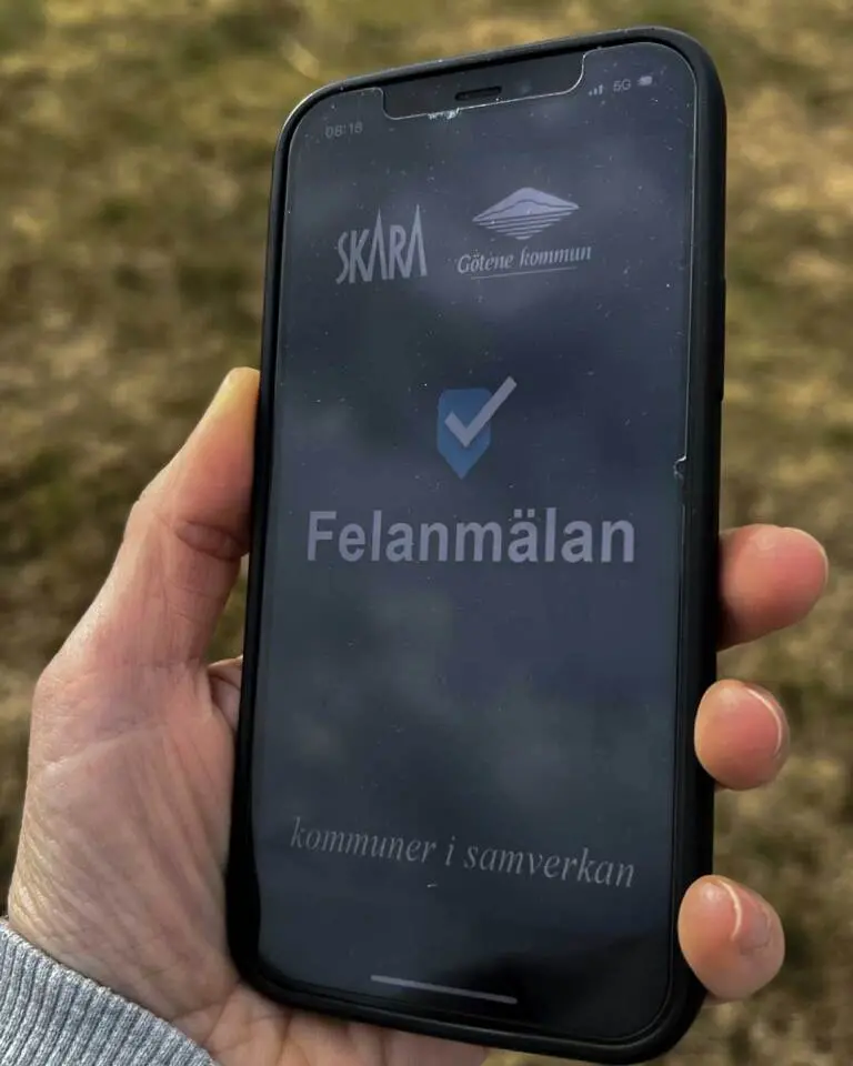 En hand som håller en smart telefon. På skärmen syns texten Felanmälan och Skara och Götene kommuners logotyper.