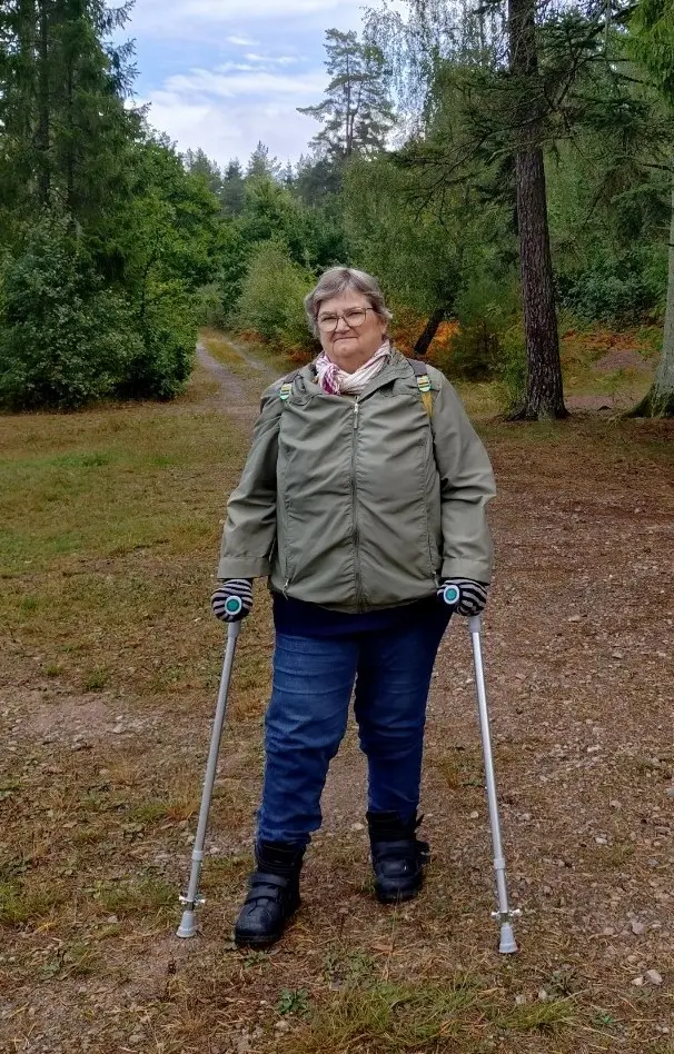 Kvinna står i en skog. Hon har kryckor.