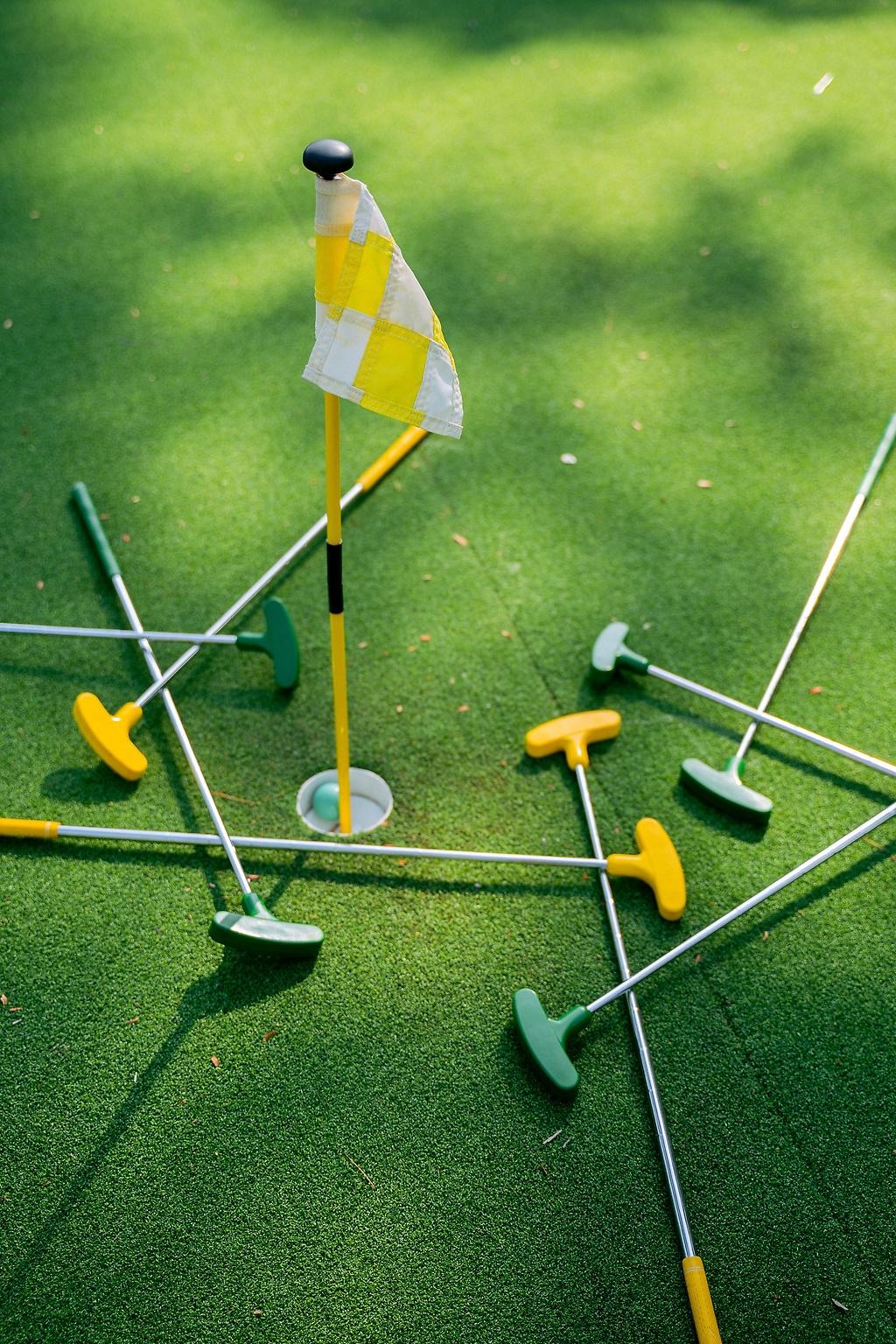 En liten flagga samt några stålgolfklubbor liggandes på en grön konstgräsmatta