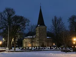 Forshems kyrka i vintermotiv med snö och tända lycktor och ljus.