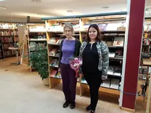 Två kvinnor som står framför en bokhylla i ett bibliotek.