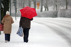 Två kvinnor går på en gata när det snöar, den ena har ett rött paraply.