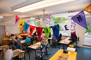 Ett klassrum med elever och färgglada vimplar i förgrunden som det står välkommen på.