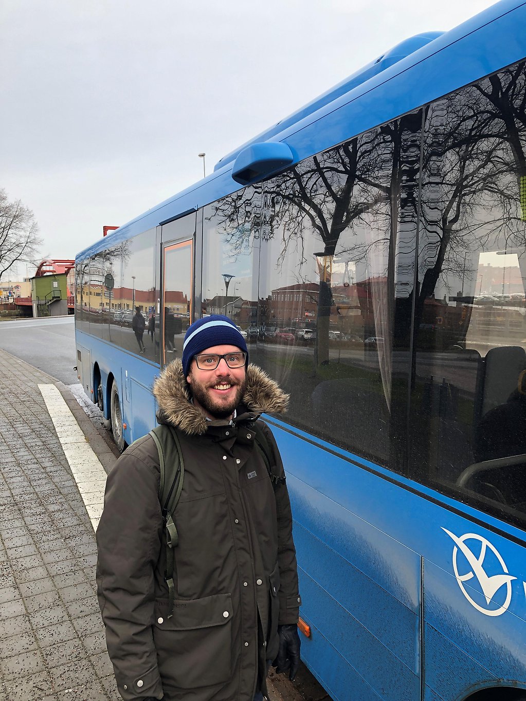 Glad man stående framför en blå buss.