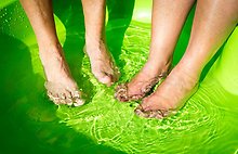 Två par fötter i en grön balja med vatten.