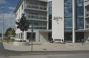 Framsidan av byggnaden Heldesborg i centrala Götene, en vitputsad byggnad med stora glasfönster.