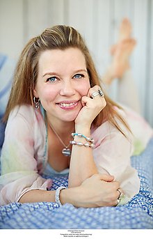 Blond kvinna som ligger på mage på en filt och ler in i kameran.