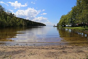 Badplats Kinnekulle Camping en beige sandstrand med vattnet intill stranden. Blå himmel.