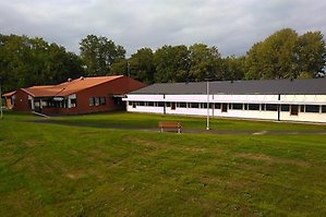 Tegelbyggnad och lägre vit byggnad med grönt gräs i förgrunden.