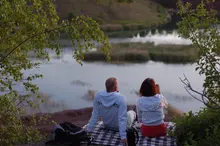 Ett par, en man och en kvinna, sitter på en filt och tittar ut över en sjö.