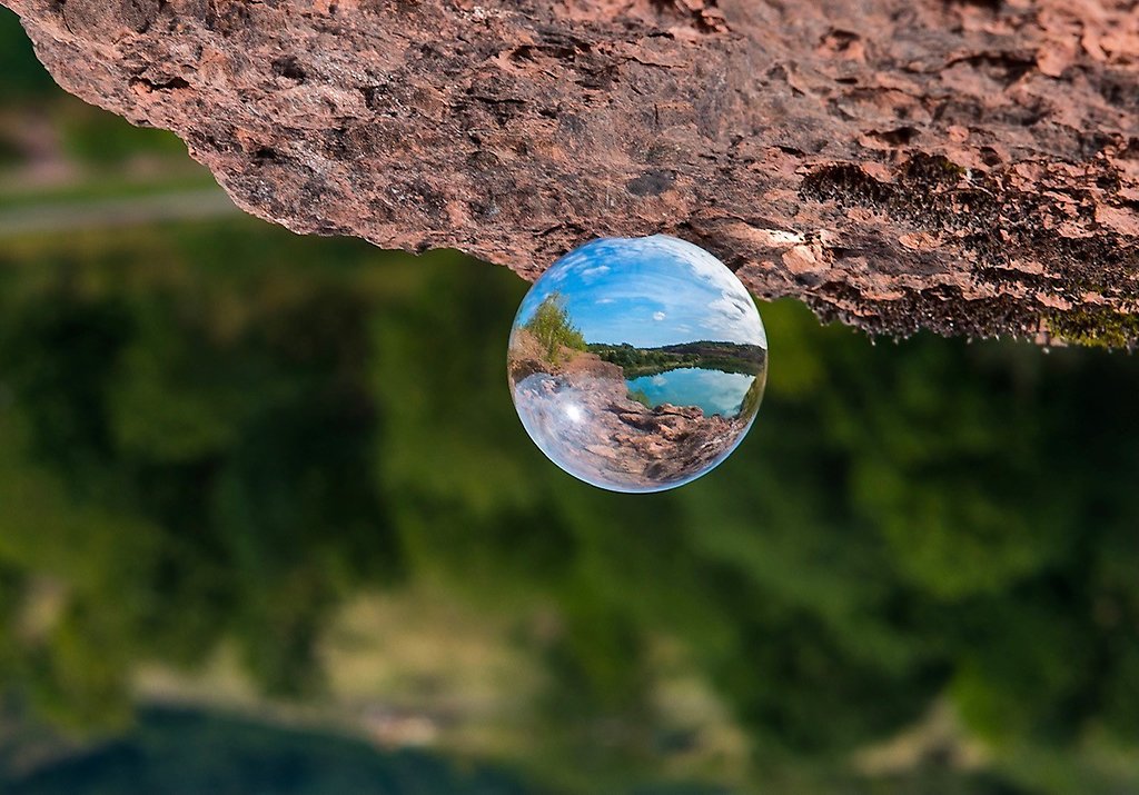 En glaskula som reflekterar vattnet vid stora stenbrottet, placerad på en klippa. 