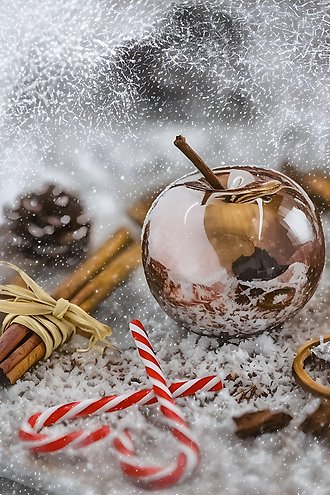 Ett vitt frostigt bord med vitrödrandiga godiskäppar, bruna kanelpinnar och ett stort genomskinligt äpple.