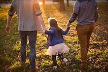 Bild på två vuxna och ett barn som håller varandra i händerna.