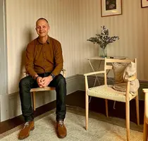 En man sitter på en stol, brevid honom står en tom stol.