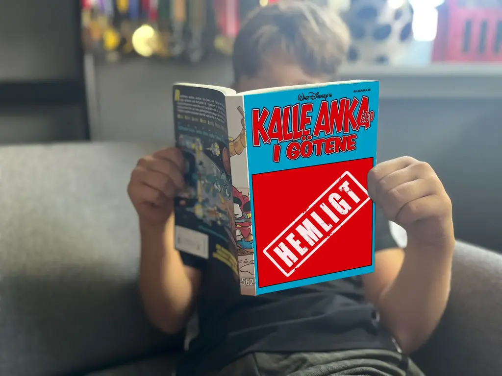 En pojke läser i en serietidning som heter "Kalle Anka i Götene". Med en ruta över framsidan med en stämpel där det står "Hemligt".