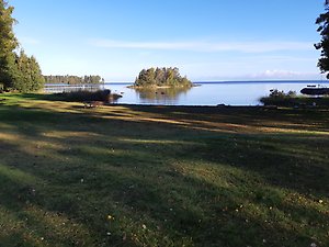 Jutevikens badplats, en grön gräsyta intill vattnet med en klarblå himmel.