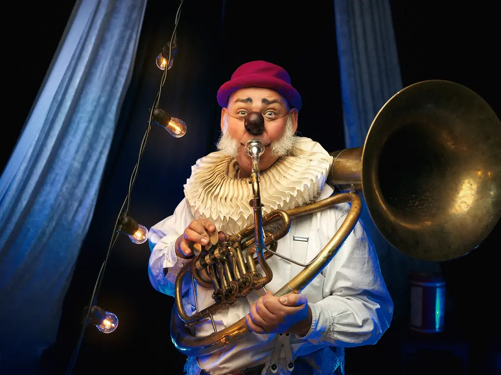 En man utklädd till clown som står och blåser i en bastuba.