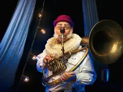 En man utklädd till clown som står och blåser i en bastuba.