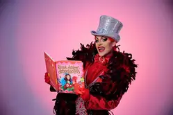 Dragqueen med rött hår som läser i en sagobok för barn.