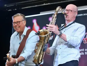 Två män som spelar gitarr och saxofon på en scen.