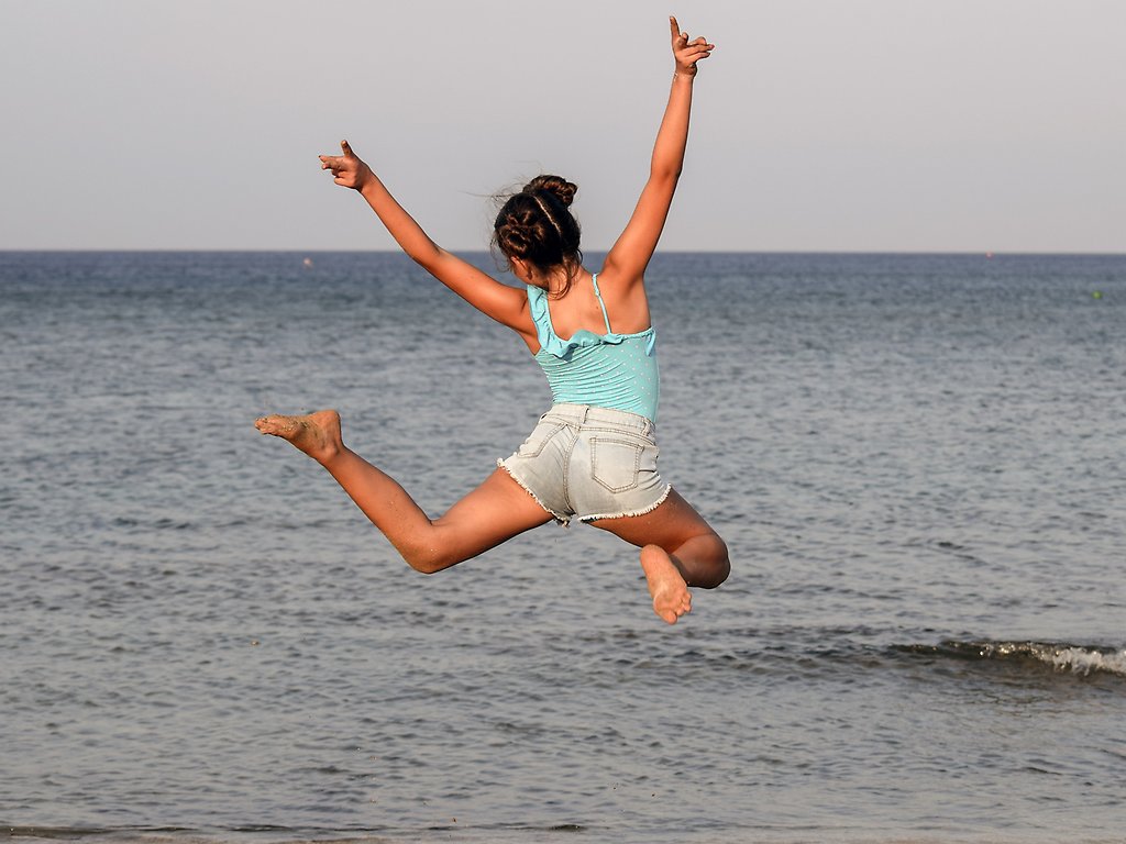 Flicka som hoppar vid vattnet på en strand.