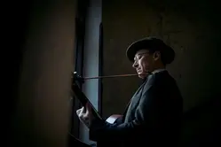 Man i hatt står vid en fönster och spelar gitarr.