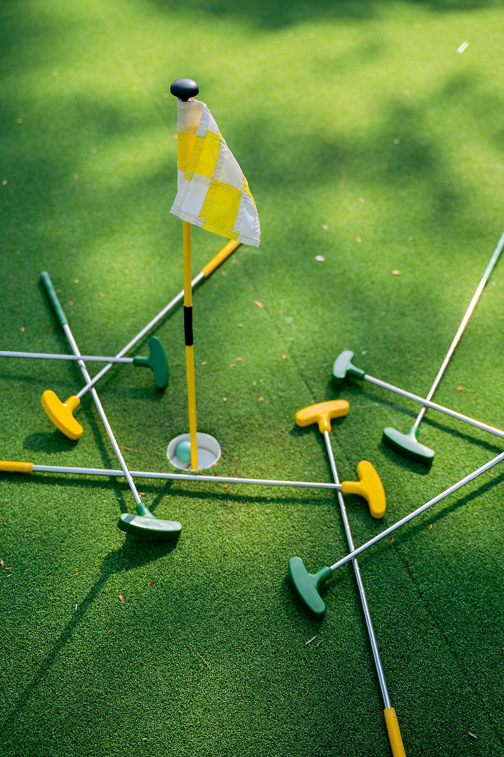 Gula och gröna minigolfklubbor ligger ner på grönt konstgräs.