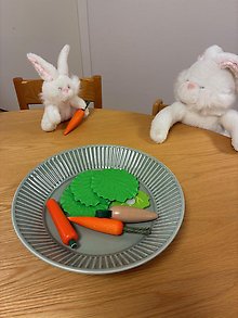 Bild på två kaniner vid ett runt bord och sallad och morötter.