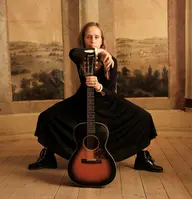 Kvinna som sitter bakom en gitarr.