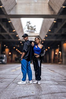 En kille med keps och skjorta i svart ståt tillsammans med en långhårig tjej med blått linne.