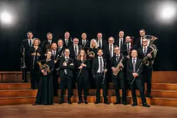 En grupp människor i mörka kläder står på en scen och håller i olika blåsinstrument.