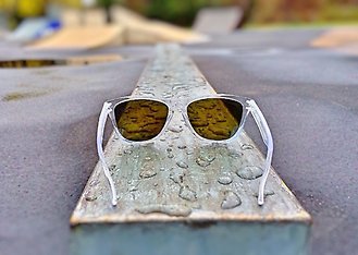 Ett par solglasögon liggandes på en planka med regndroppar.