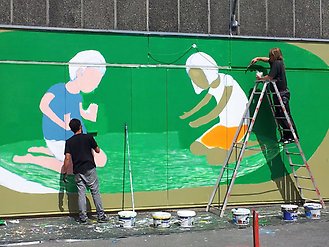 Två personer som målar på en vägg. Man ser konturerna av två barn mot grön bakgrund.