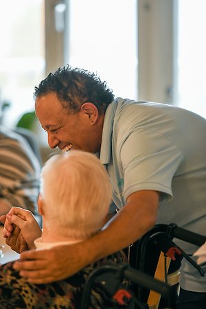 Omsorgspersonal sitter med en äldre dam vid ett fikabord