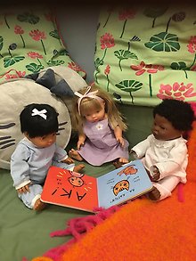 Tre dockor sitter i en soffa och tittar i en pekbok.
