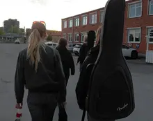 Fyra tjejer som går på en parkering. Två av dem bär gitarrer på ryggen.