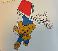 Bild på Bamse som springer med en drake som Lille Skutt håller sig i.