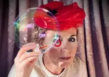 Bild på en kvinna med röd hatt som tittar genom en såpbubbla hon just blåst.