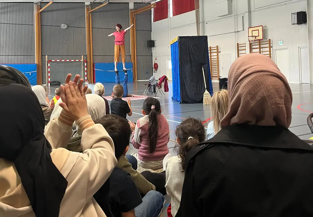 Ryggar på publik inne i en idrottshall som tittar på en cirkusföreställning där akrobatik görs.