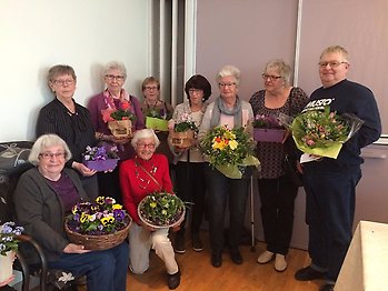En grupp med 9 män och kvinnor står uppställda med blommor i händerna.