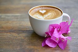 En kaffekopp med en lila blomma bredvid på ett träbord