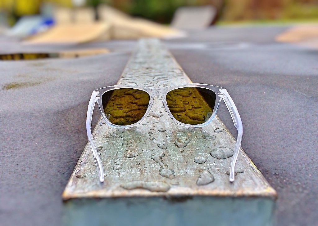 Ett par solglasögon som ligger på en planka med vattendroppar på.