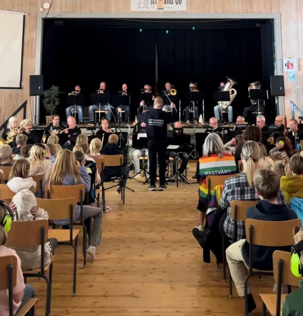 En orkester spelar framför en publik med barn som sitter på stolar.