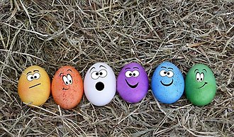 Sex stycken färgglada ägg med olika ansiktsuttryck liggandes på hö.