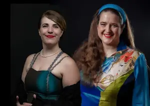 Två kvinnor står bredvid varandra och ler mot en helt svart bakgrund.