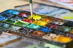 Akvarellfärger och pensel som ligger bredvid varandra.